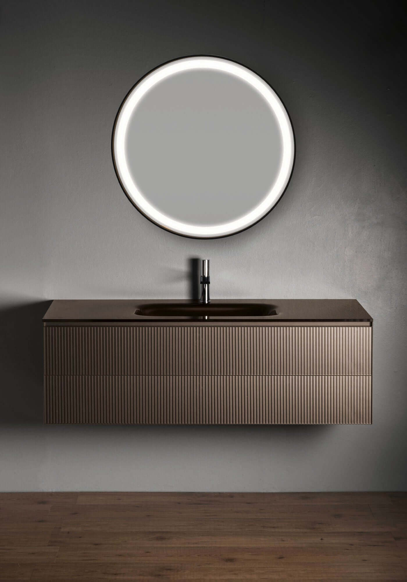 Modern brown bathroom vanity with a single basin, aluminum handle-frame, and a round mirror above it, set against a dark background.