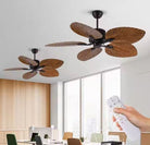Two ceiling fans with wooden blades in a room with large windows and a hand holding a remote control.