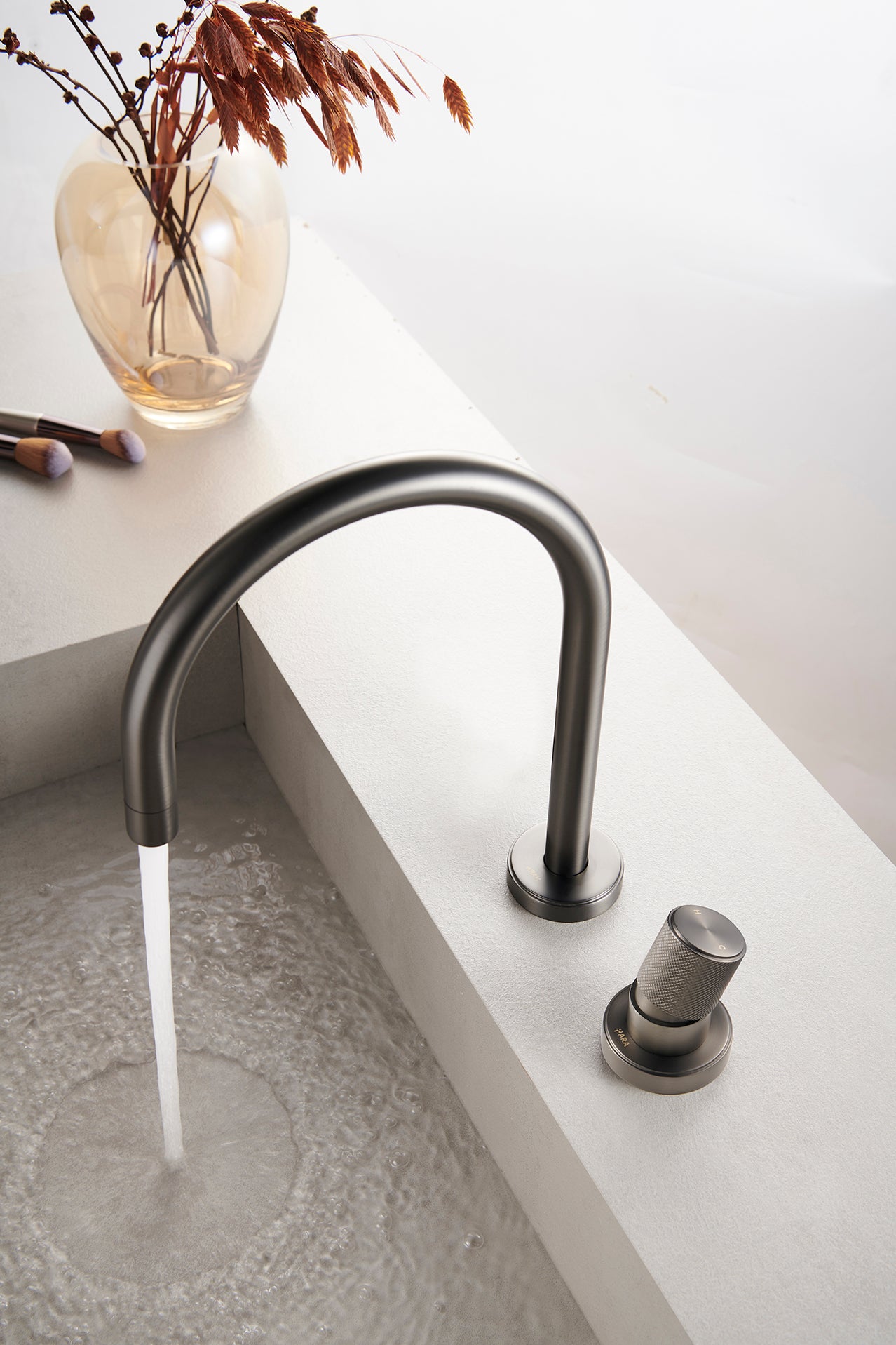 Modern gunmetal faucet with water flowing into a sink on a white countertop.