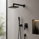 Black shower set mounted on a tiled wall with a blurred green plant in the background